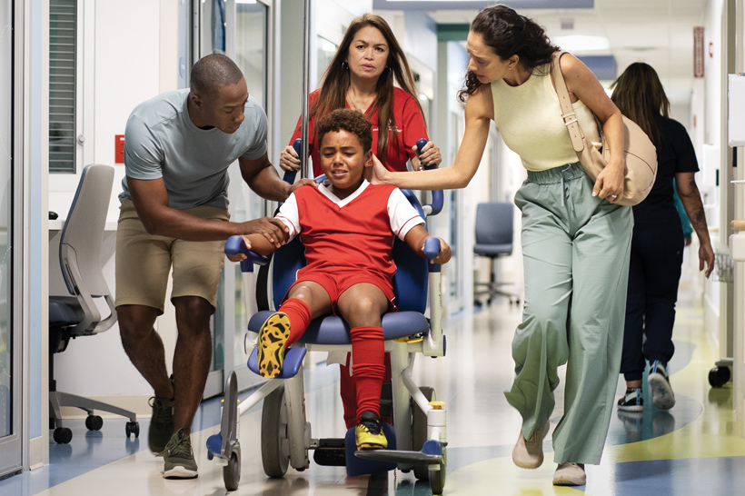 A little boy in a wheelchair being pushed by hospital staff with his parents.