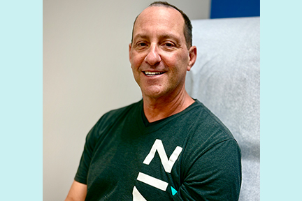 Scott, smiling warmly, sitting in an exam room.