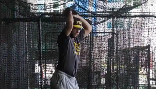 baseball player throwing ball in front of batting cage